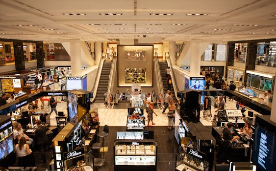 A bustling scene inside a modern shopping mall with escalators and various retail stalls.